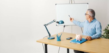 Ofiste bir sunum yapan profesyonel mali danışman ve işadamı, beyaz tahtaya işaret ediyor.