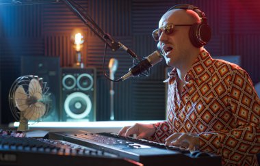 Kayıt stüdyosunda çalışan havalı sanatçı, şarkı söylüyor ve klavye çalıyor.