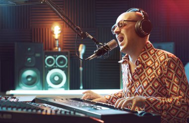 Kayıt stüdyosunda çalışan havalı sanatçı, şarkı söylüyor ve klavye çalıyor.