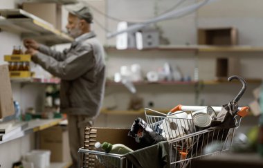 Hopeless senior disaster survivor looking for food at the destroyed abandoned supermarket: war, crisis, hunger and catastrophes concept clipart