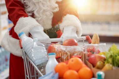 Noel Baba süpermarkette alışveriş yapıyor, alışveriş arabasını itiyor, elleri kapalı.
