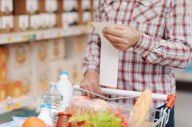 Müşteri markette uzun bir market fişini kontrol ediyor, eller kapalı.