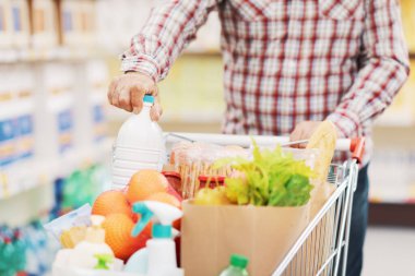 Süpermarketten alışveriş yapan adam, alışveriş arabasına bir ürün koyuyor, market alışverişi konsepti.