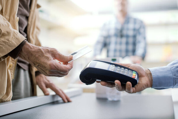 Senior man purchasing groceries at the store, he is paying using a credit card, hands close up