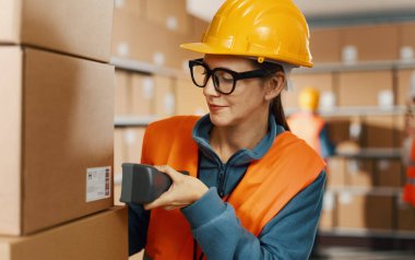 Verimli bir depo çalışanı, el tarayıcısı, lojistik ve nakliye konsepti kullanarak bir teslimat kutusu etiketindeki barkodu tarıyor.