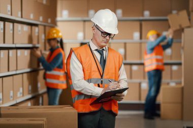 Warehouse manager posing with a clipboard, he is checking orders and doing inventory control, logistics and shipment concept clipart