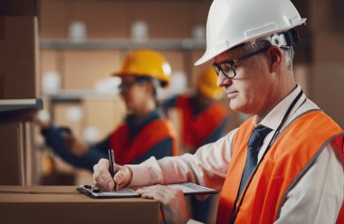 İş yerindeki profesyonel depo müdürü, bir belge yazıyor ve siparişleri kontrol ediyor: lojistik ve teslimat hizmeti kavramı