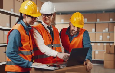 Dağıtım deposu çalışanları birlikte çalışıyor. Laptop, lojistik ve teslimat konseptinden siparişleri kontrol ediyorlar.