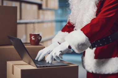 Noel Baba depoda dizüstü bilgisayarla çalışıyor. Eller yukarı.