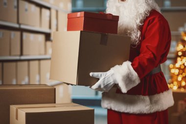 Depoda Noel Baba 'nın elinde teslimat kutuları ve Noel hediyeleri var: dağıtım hizmeti ve tatil konsepti.