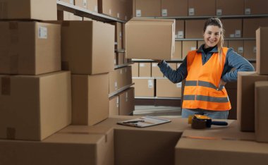 Güçlü bir kadın depo çalışanı bir eliyle kutuyu kaldırıyor ve gülümsüyor.