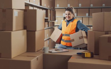 Kutuları taşıyan güçlü bir depo çalışanının portresi, kameraya gülümsüyor.