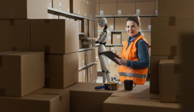 Kadın ve android yapay zeka robotu bir depoda birlikte çalışıyorlar. Kadın bir panoda siparişi kontrol ediyor ve gülümsüyor.