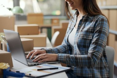 Bilgisayarla çalışan bir e-ticaret uzmanı, arka planda teslimat kutuları, sevkiyat ve perakende konsepti