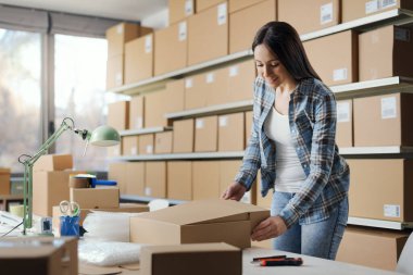 Kadın bir teslimat kutusunu kapatıp sevkiyat hazırlıyor: e-ticaret, sevkiyat ve teslimat konsepti.