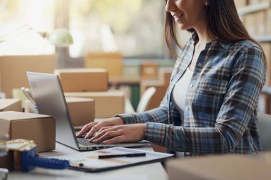 Bilgisayarla çalışan bir e-ticaret uzmanı, arka planda teslimat kutuları, sevkiyat ve perakende konsepti