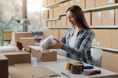 E-ticaret işyeri sahibi dükkanında çalışıyor. Malları baloncuklu ambalajla paketliyor.