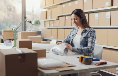 E-ticaret işyeri sahibi dükkanında çalışıyor. Malları baloncuklu ambalajla paketliyor.
