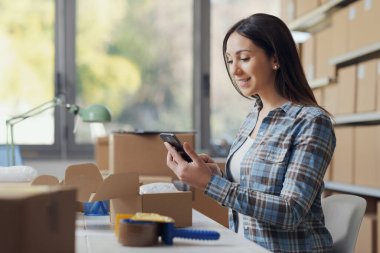 Gülümseyen bir e-ticaret şirketi sahibi masada oturuyor ve akıllı telefon, teknoloji ve iletişim konsepti kullanıyor.