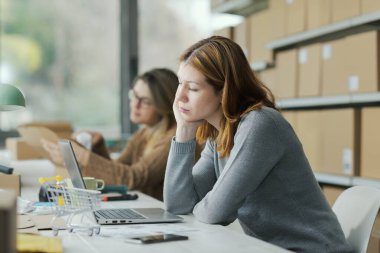 Düşünceli, yorgun genç bir kadın ofis masasında oturuyor ve depresyonda olduğunu ve sıkıldığını düşünüyor.