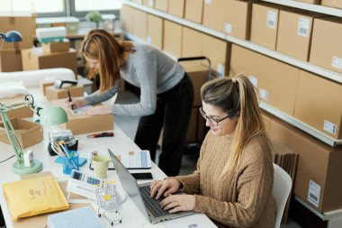 Bir e-ticaret mağazası işleten ve birlikte çalışan genç girişimci kadınlar, bir dizüstü bilgisayardan siparişleri kontrol ediyorlar ve sevkiyatları hazırlıyorlar.