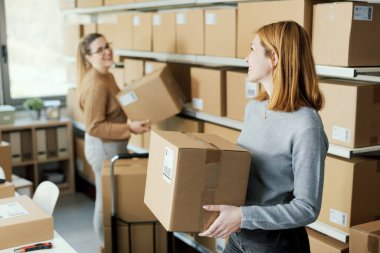 Gülümseyen depo çalışanları teslimat kutularını raflara, e-ticaret ve dağıtım konseptine koyuyorlar.