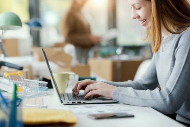 Genç bir e-ticaret çalışanı masada oturuyor ve bir dizüstü bilgisayarda daktilo yazıyor.