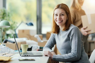 Ofis masasında oturmuş kameraya gülümseyen bir e-ticaret çalışanının portresi.