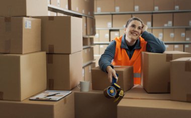 Mola verip karton kutulara yaslanan mutlu bir depo çalışanı düşünüyor ve başka tarafa bakıyor.