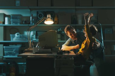 Garajda eski bir bilgisayar kullanarak ve video oyunları oynayarak mutlu bir baba-oğul kutluyor.