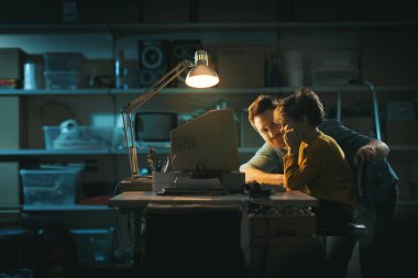 Garajda genç bir baba ve çocuk, eski bir bilgisayar kullanıyorlar ve birlikte oynuyorlar, aile ve birliktelik kavramı.