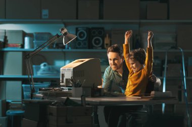 Garajda eski bir bilgisayar kullanarak ve video oyunları oynayarak mutlu bir baba-oğul kutluyor.