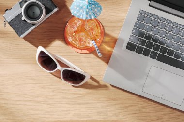 Masadaki dizüstü bilgisayar, kamera, kokteyl ve güneş gözlükleri: yaz tatilleri ve rahatlama konsepti, üst görünüm