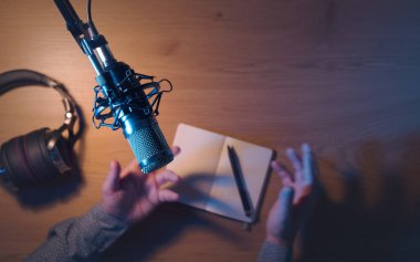 Profesyonel içerik yaratıcısı ve etkili kişi canlı yayında bir podcast yayınlıyor, mikrofona konuşuyor ve ellerini hareket ettiriyor, üst görünüm