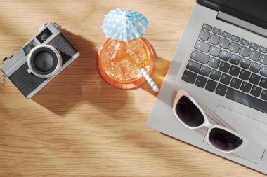 Masadaki dizüstü bilgisayar, kamera, kokteyl ve güneş gözlükleri: yaz tatilleri ve rahatlama konsepti, üst görünüm