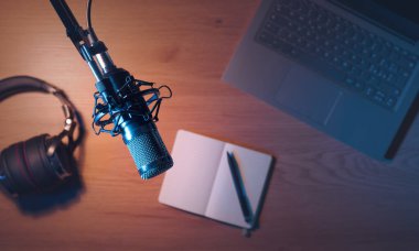 Podcaster work desk with professional equipment: microphone, laptop, headphones and notebook, top view clipart