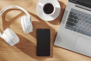 Ev ofisinin ahşap masasında dizüstü bilgisayarı, kahvesi ve kişisel eşyaları var.