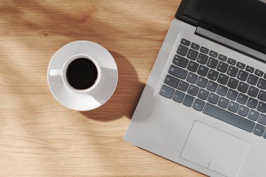 Ev ofisinin ahşap masasında dizüstü bilgisayarı, kahvesi ve kişisel eşyaları var.