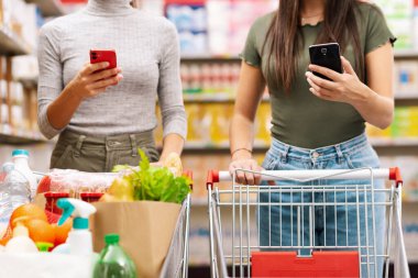 Gençler süpermarkette alışveriş yapıyor ve akıllı telefonlarını kullanıyorlar.