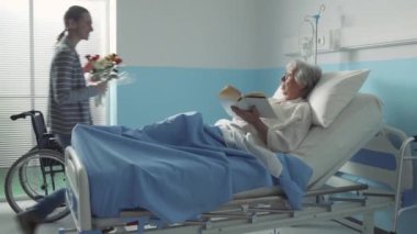 Hasta annesini ziyarete gelen genç bir kadın hastane yatağında yatıyor, birlikte konuşuyor ve gülümsüyorlar.