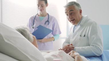 Hasta annesini ziyarete gelen genç bir kadın hastane yatağında yatıyor, birlikte konuşuyor ve gülümsüyorlar.