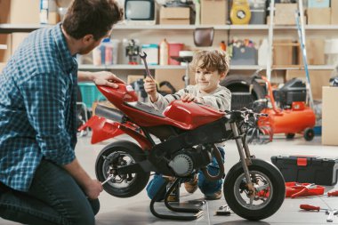 Genç baba garajda oğlunun motosikletini kontrol ediyor, çocuk ona yardım ediyor ve aile ve birliktelik kavramını öğreniyor.