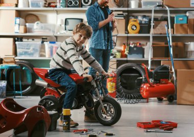 Bakıcı baba garajda oğlunun motosikletini kontrol ediyor. Aile ve birliktelik kavramı.