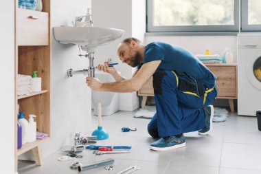 Profesyonel tesisatçı banyo lavabosunu tamir ediyor, su pompası kullanarak boru tamir ediyor.