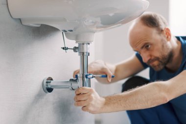 Lavabo giderinde çalışan uzman tesisatçı, su pompası kullanıyor ve boru tamir ediyor.