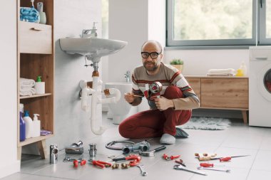 Inexpert confused man fixing the bathroom sink drain by himself, he is using adhesive tape to repair and join the pipes clipart