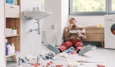 Umutsuz bir adam banyoda yerde oturuyor. Alet edevat ve borularla kuşatılmış. Lavabosunu tamir edemiyor.