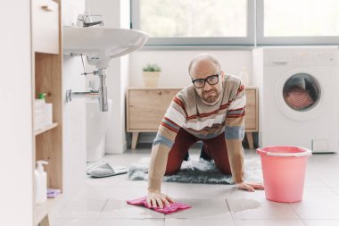 Banyodaki ıslak zemini temizleyen adam, lavabo sızdırıyor.