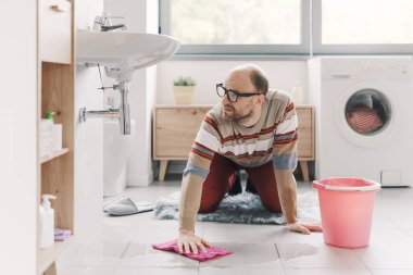 Banyodaki ıslak zemini temizleyen adam, lavabo sızdırıyor.