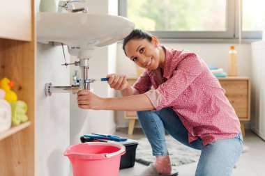 Becerikli genç kadın banyo lavabosunu kendi başına tamir ediyor. Su pompası kullanıyor.